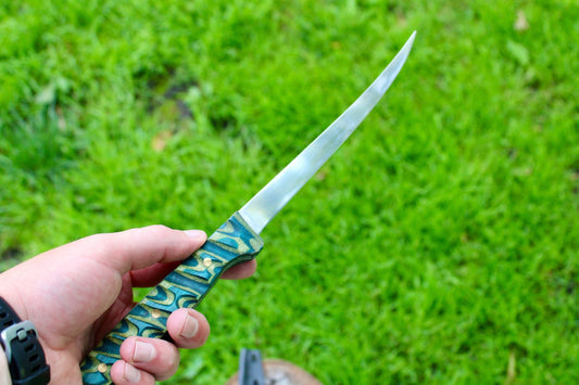 Hand holding a decorative knife with a green and gold handle against a grassy background